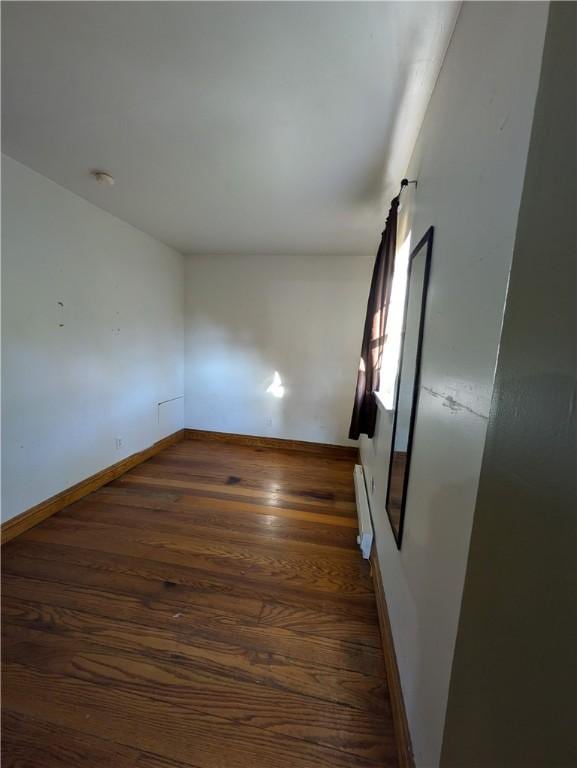 empty room featuring dark wood-type flooring and a baseboard radiator