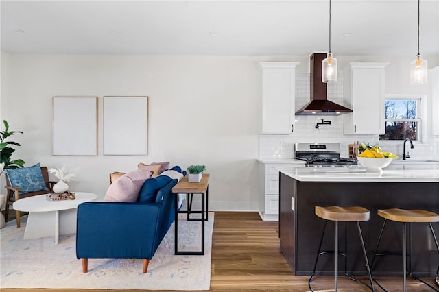 kitchen featuring white cabinetry, wall chimney exhaust hood, stainless steel range with gas cooktop, wood-type flooring, and decorative light fixtures