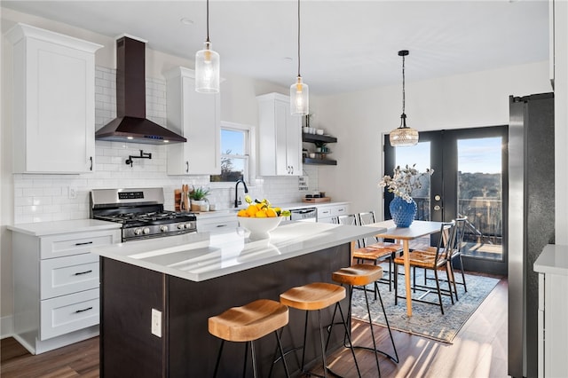 kitchen featuring wall chimney exhaust hood, a healthy amount of sunlight, white cabinetry, and appliances with stainless steel finishes