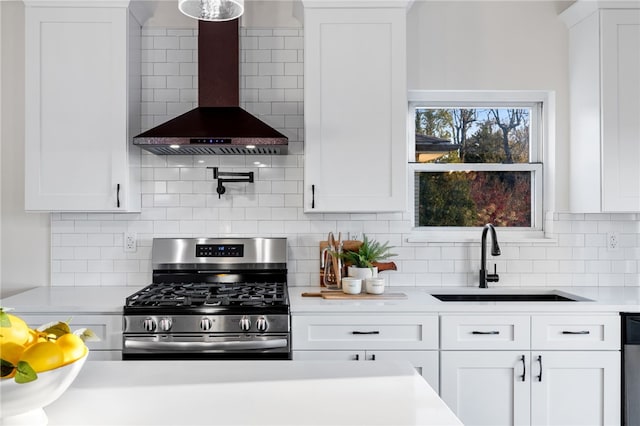 kitchen featuring white cabinets, wall chimney range hood, sink, gas range, and decorative backsplash