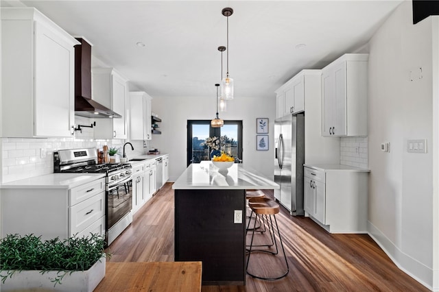 kitchen with wall chimney range hood, sink, appliances with stainless steel finishes, a kitchen island, and white cabinetry