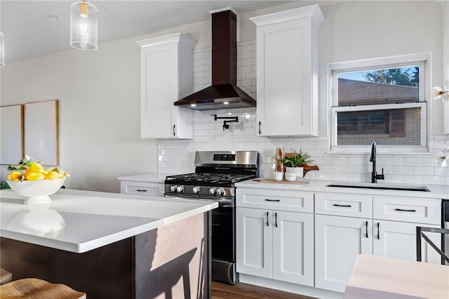 kitchen with backsplash, sink, wall chimney exhaust hood, gas stove, and white cabinetry