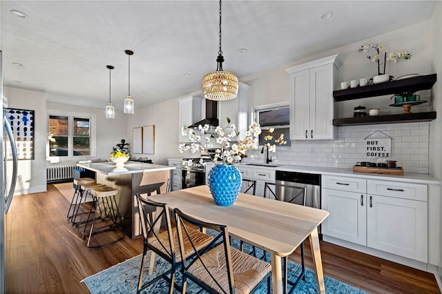 kitchen featuring white cabinets, radiator, hanging light fixtures, and wall chimney range hood