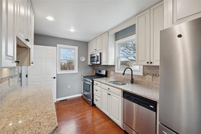 kitchen with dark wood-type flooring, white cabinets, sink, light stone countertops, and appliances with stainless steel finishes