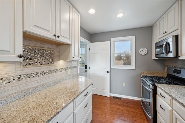 kitchen featuring white cabinetry, dark wood-type flooring, stainless steel appliances, light stone counters, and decorative backsplash