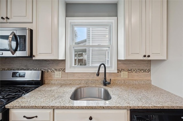 kitchen with decorative backsplash, appliances with stainless steel finishes, light stone counters, sink, and white cabinetry