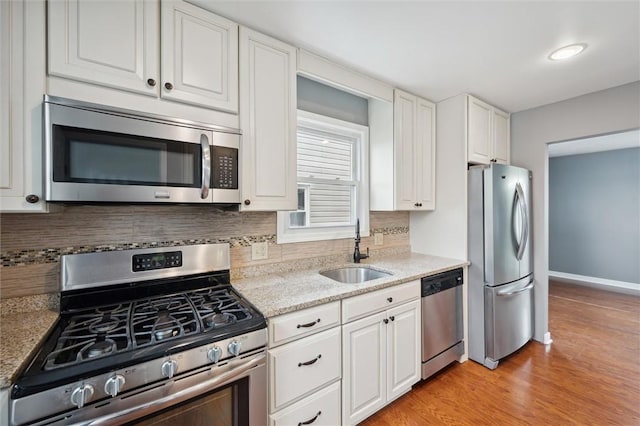 kitchen featuring light stone counters, stainless steel appliances, sink, light hardwood / wood-style floors, and white cabinetry