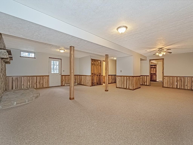 basement featuring wood walls, carpet, a textured ceiling, and ceiling fan