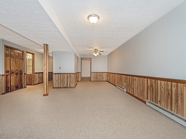 basement with a textured ceiling, light colored carpet, ceiling fan, and a baseboard heating unit