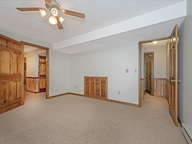 empty room with ceiling fan, a baseboard radiator, wood walls, light colored carpet, and a textured ceiling