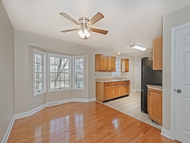 kitchen featuring ceiling fan, sink, black fridge, light hardwood / wood-style floors, and a textured ceiling