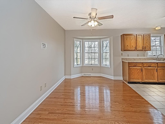 kitchen with a textured ceiling, ceiling fan, light wood-type flooring, and sink