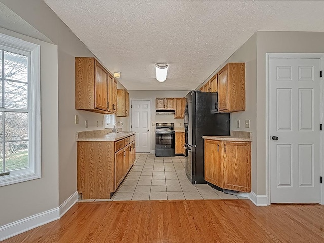 kitchen featuring sink, black appliances, a textured ceiling, and light hardwood / wood-style floors