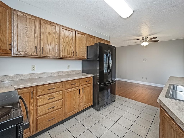 kitchen with black fridge, a textured ceiling, ceiling fan, range, and light hardwood / wood-style floors