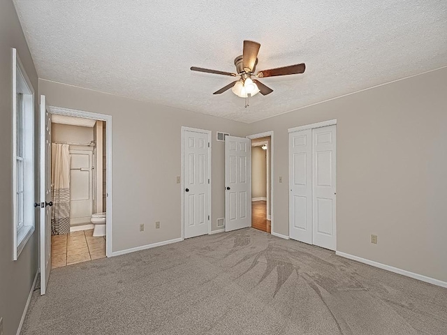 unfurnished bedroom featuring a textured ceiling, light colored carpet, ceiling fan, and ensuite bathroom