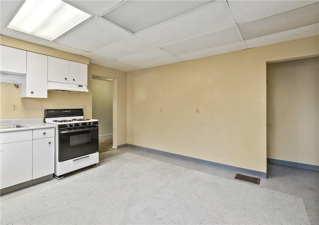 kitchen with white cabinets, a drop ceiling, white gas stove, and sink