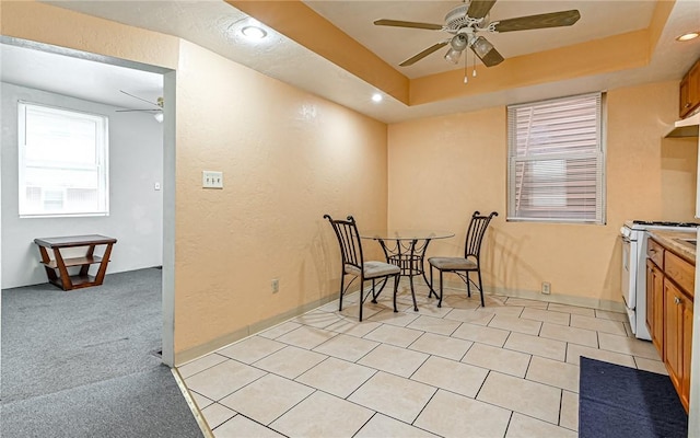 dining room featuring ceiling fan, light colored carpet, and a tray ceiling