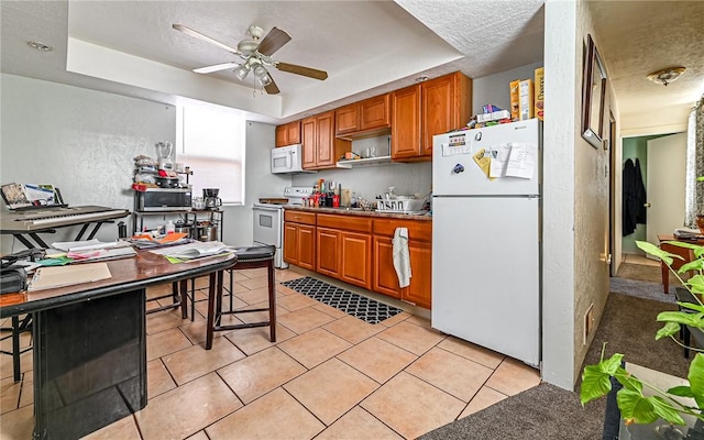 kitchen featuring a kitchen bar, white appliances, a raised ceiling, ceiling fan, and light tile patterned flooring