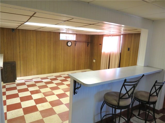 kitchen with kitchen peninsula, a kitchen breakfast bar, a drop ceiling, and wooden walls