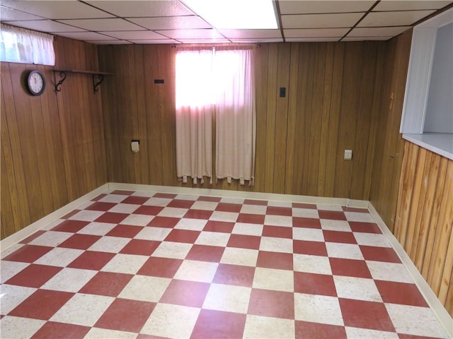 basement with a paneled ceiling and wood walls