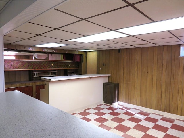 kitchen featuring kitchen peninsula, wooden walls, and a drop ceiling