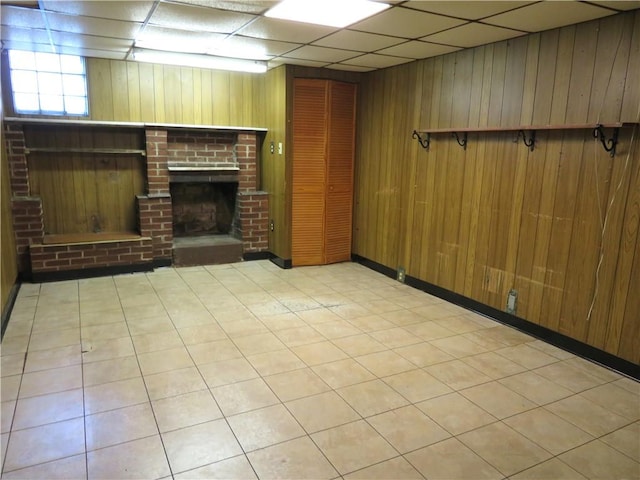 basement featuring a paneled ceiling, wood walls, and a brick fireplace