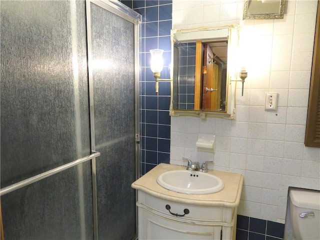 bathroom with vanity, toilet, a shower with door, and tile walls