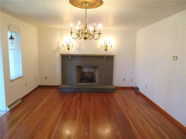 unfurnished living room with a stone fireplace, an inviting chandelier, a baseboard heating unit, and hardwood / wood-style flooring