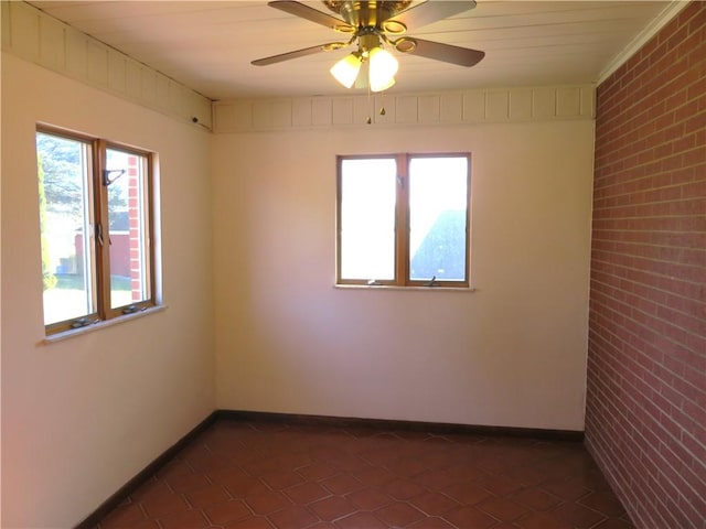 unfurnished room featuring ceiling fan, brick wall, and dark tile patterned flooring