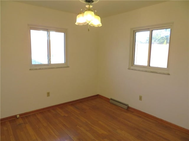 empty room featuring wood-type flooring, a baseboard heating unit, and a notable chandelier