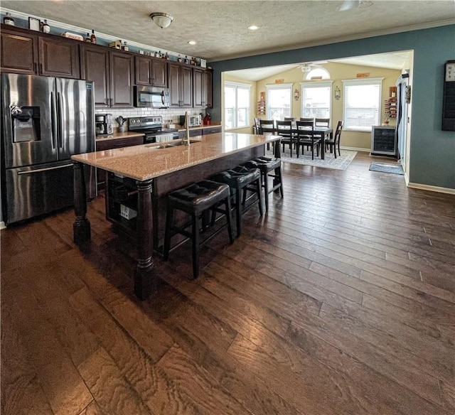 kitchen featuring a breakfast bar, a center island with sink, a textured ceiling, appliances with stainless steel finishes, and dark brown cabinetry