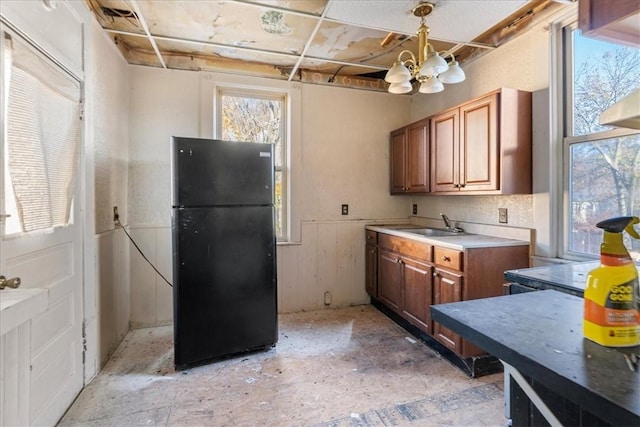 kitchen with hanging light fixtures, black refrigerator, a chandelier, and sink