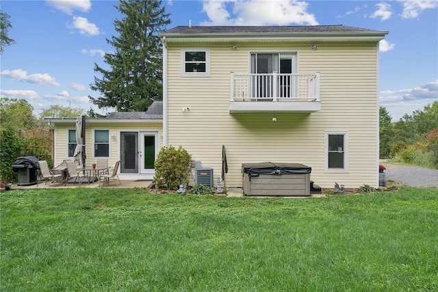 rear view of house with a balcony, a patio area, a yard, and a hot tub