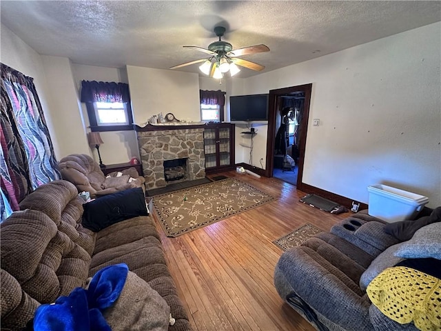 living room featuring a stone fireplace, ceiling fan, wood-type flooring, and a textured ceiling