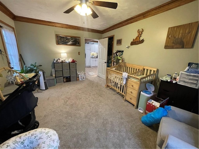 carpeted bedroom with a nursery area, ceiling fan, and ornamental molding