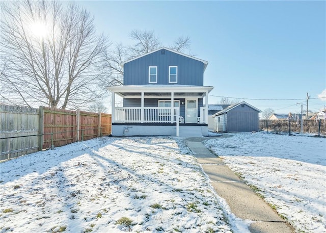 snow covered rear of property featuring covered porch and a storage shed