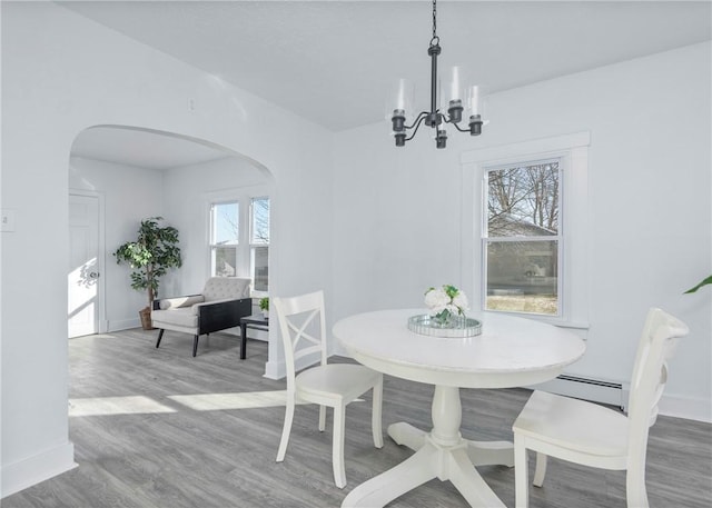 dining area with baseboard heating, an inviting chandelier, a healthy amount of sunlight, and wood-type flooring