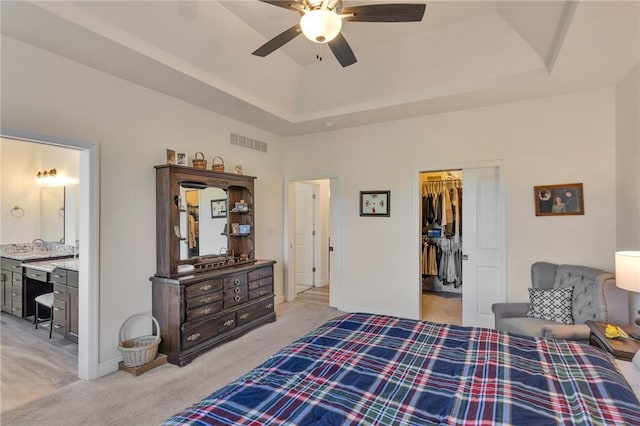 carpeted bedroom featuring ensuite bathroom, a raised ceiling, a walk in closet, ceiling fan, and a closet