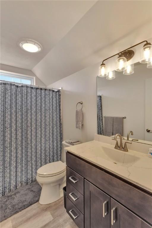 bathroom featuring hardwood / wood-style floors, vanity, toilet, and lofted ceiling