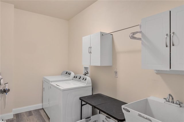 clothes washing area featuring washing machine and clothes dryer, sink, cabinets, and light hardwood / wood-style flooring