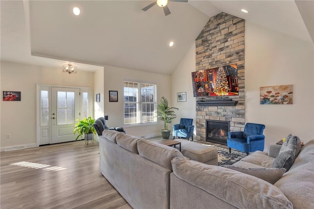 living room featuring a stone fireplace, ceiling fan, high vaulted ceiling, and light hardwood / wood-style floors