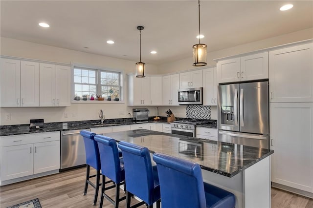 kitchen with stainless steel appliances, sink, decorative light fixtures, white cabinets, and a center island