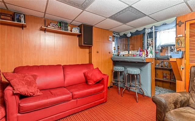 carpeted living room with wood walls and a drop ceiling