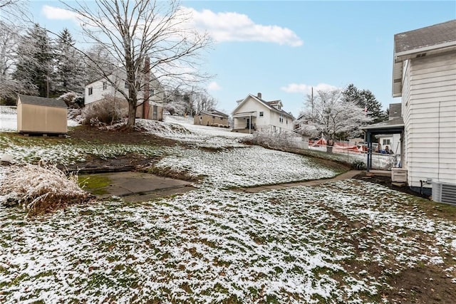 snowy yard with central AC and a shed