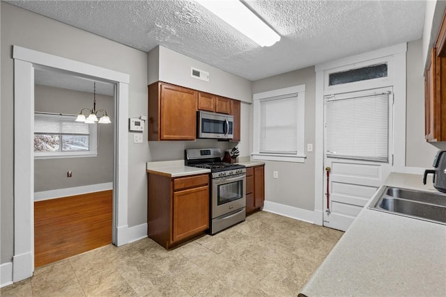 kitchen with a notable chandelier, pendant lighting, a textured ceiling, and appliances with stainless steel finishes