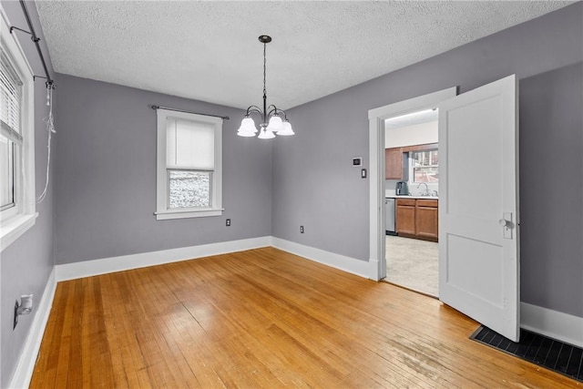 empty room with a textured ceiling, light hardwood / wood-style flooring, a notable chandelier, and sink