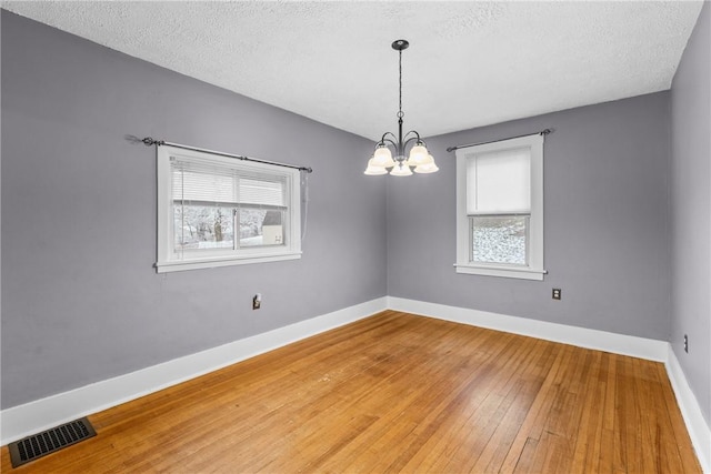 unfurnished room with wood-type flooring, a textured ceiling, an inviting chandelier, and a wealth of natural light