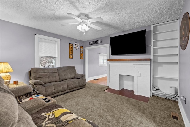 living room with carpet, ceiling fan, a textured ceiling, and a brick fireplace