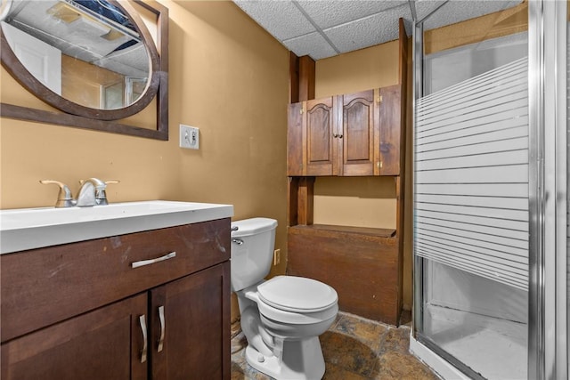 bathroom featuring vanity, toilet, a shower stall, stone finish floor, and a drop ceiling