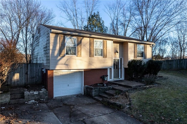 raised ranch featuring concrete driveway, brick siding, fence, and an attached garage
